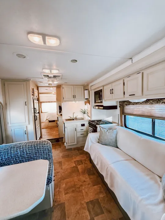 Bright RV rental interior showing a full kitchen, seating area with sofa, and dining booth in light colors and wood floors.. Forest River Sunseeker 2015