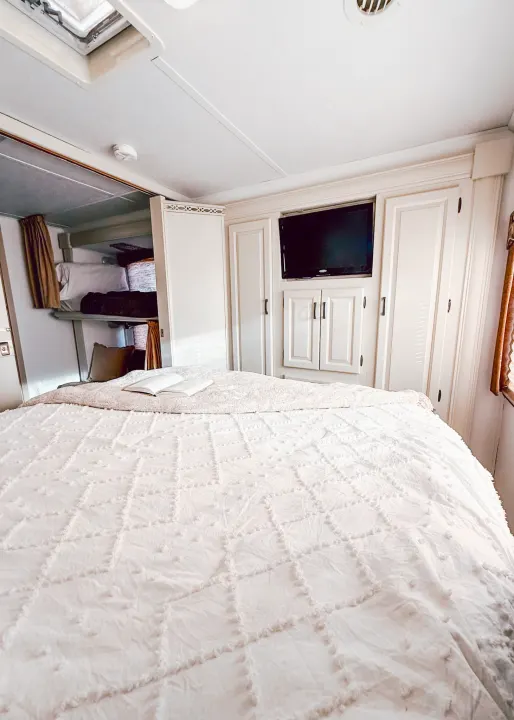 Inside a cozy RV rental bedroom: a large textured bed, open book, built-in storage, TV, and bunk beds.. Forest River Sunseeker 2015