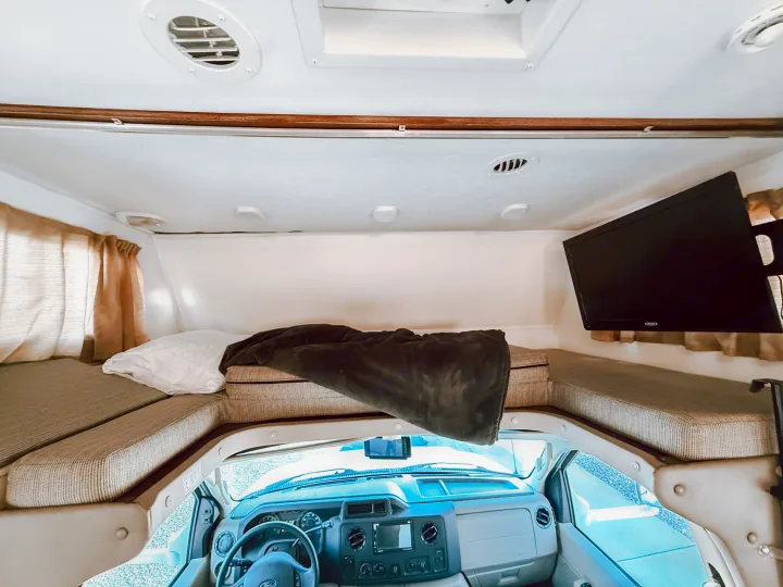 Inside an RV rental looking forward: large cab-over bunk bed, driver's dashboard, and right-side wall TV.. Forest River Sunseeker 2015