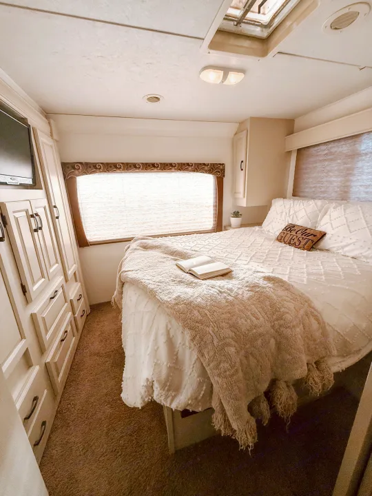 Cozy RV rental bedroom with white bedding, "Be Our Guest" pillow, TV, and ample storage for travel.. Forest River Sunseeker 2015