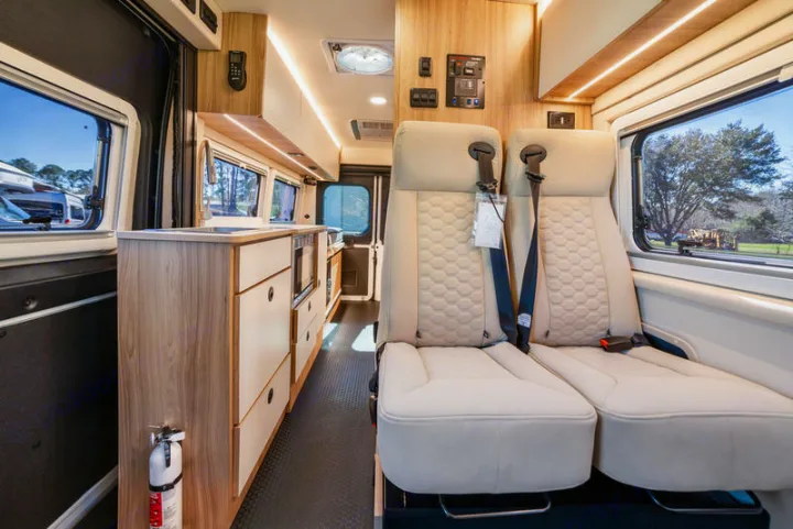 Explore this modern RV rental camper van interior, featuring a sleek kitchen area, comfortable beige seating, and large windows.. Coachmen PIXEL 2026