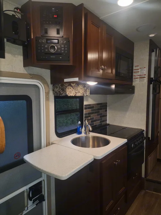 View of an RV rental's kitchen featuring a sink, stove, microwave, and essential control panel. Compact and ready for travel.. Forest River Forester 2018