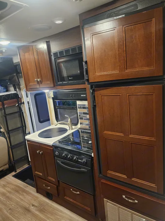 View of a well-equipped RV rental kitchen featuring a microwave, oven, sink, and large refrigerator.. Forest River Forester 2018