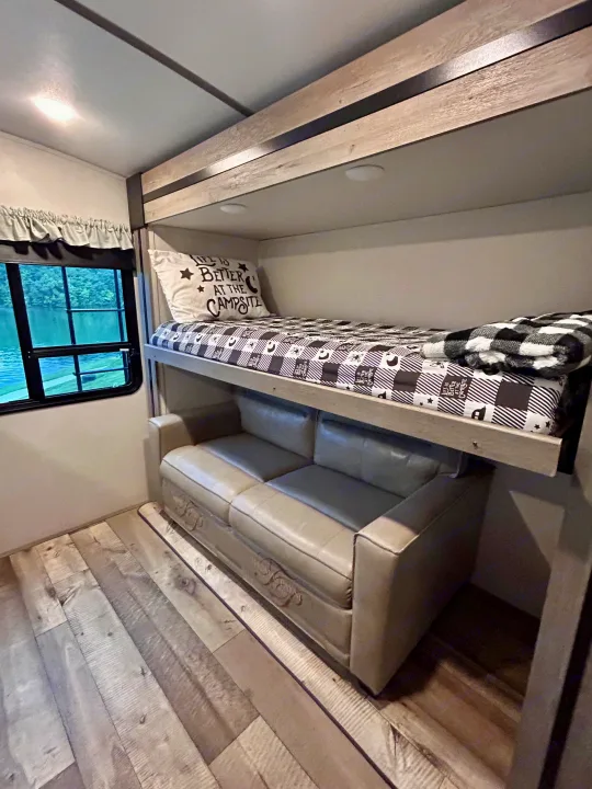 Spacious RV rental interior with bunk beds, a cozy sofa below, and a beautiful lake view from the window. Perfect for camping adventures!. Keystone RV Outback 2021