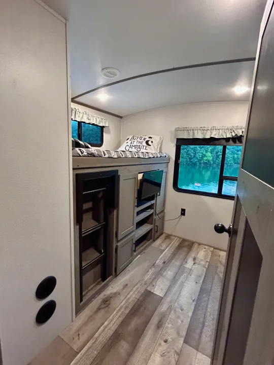 Cozy RV rental bunkhouse with lake views. Features sleeping area, TV lounge, and rustic decor, perfect for camping adventures.. Keystone RV Outback 2021