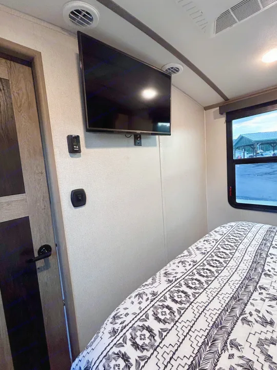 Cozy RV rental bedroom featuring a wall-mounted TV, comfy bed, and modern amenities for your travel adventures.. Keystone RV Outback 2021