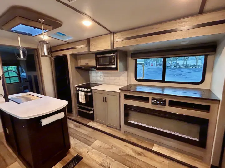 This inviting RV rental showcases a modern interior with a kitchen island, stove, microwave, and electric fireplace.. Keystone RV Outback 2021