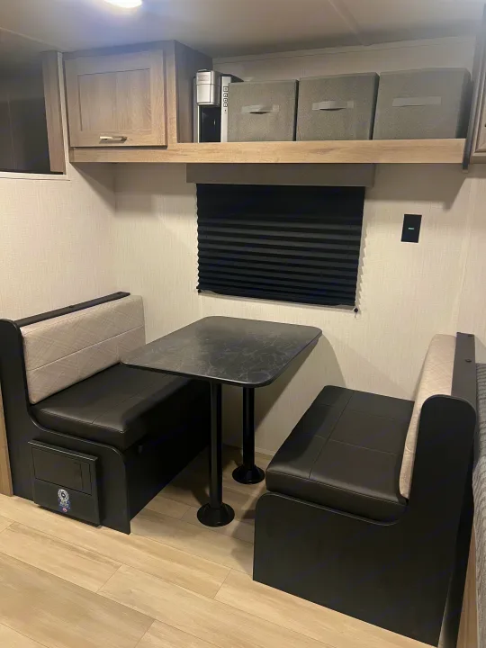 Step inside this RV rental's cozy dinette with black benches, a modern table, and overhead storage, perfect for meals on the road.. Heartland Prowler Lynx 17BHX 2025