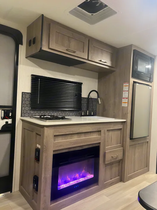 Compact RV rental kitchen interior with sink, stovetop, microwave, and electric fireplace.. Heartland Prowler Lynx 17BHX 2025