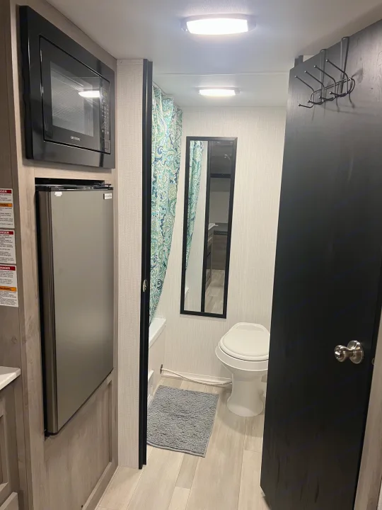 This RV rental features a small kitchen with microwave and fridge, and an attached bathroom with toilet, shower, and mirror.. Heartland Prowler Lynx 17BHX 2025