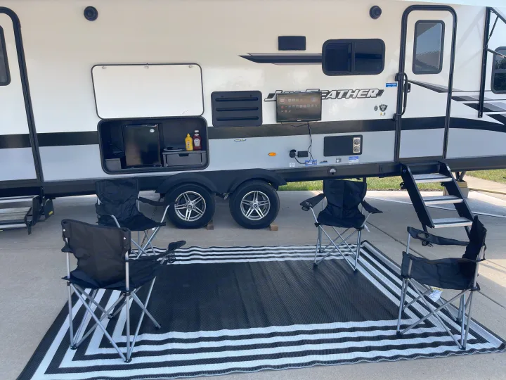 Relaxing outdoor RV setup with kitchen, TV, and comfortable chairs on a striped mat. Perfect for an RV rental adventure.. Jayco Jay Feather 2022