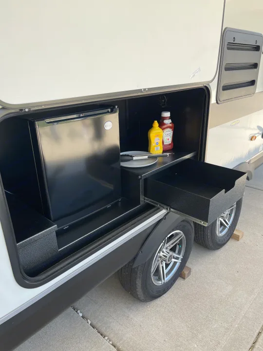 RV rental with open external storage revealing an outdoor kitchen: mini-fridge, condiments, and pull-out drawer.. Jayco Jay Feather 2022