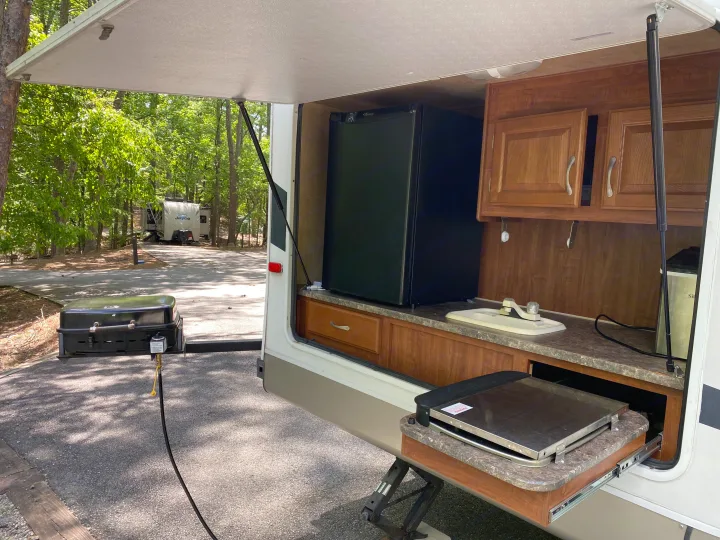 RV rental outdoor kitchen setup: fridge, sink, pull-out griddle, & gas grill for camping at a wooded site.. Jayco Eagle Super Lite 2010