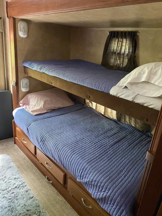 Cozy bunk beds inside an RV rental, featuring blue quilts, pillows, built-in storage drawers, and reading lights for a comfortable mobile stay.. Jayco Eagle Super Lite 2010