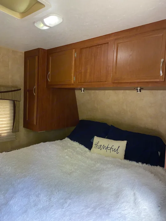 Comfortable RV rental bedroom featuring a plush white comforter, navy pillows, and overhead wooden storage.. Jayco Eagle Super Lite 2010