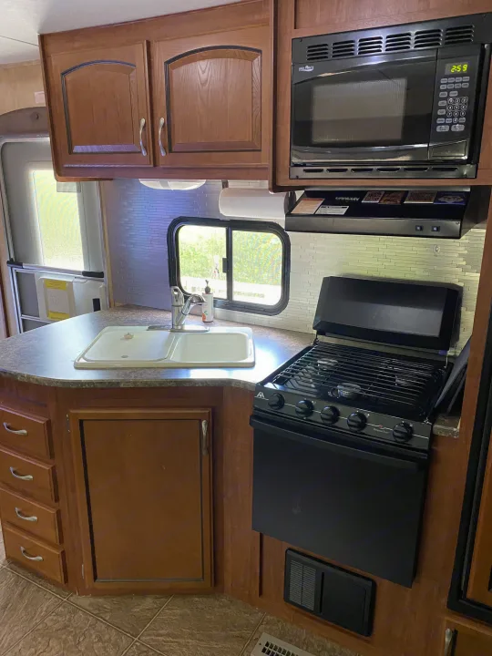 Compact RV rental kitchen featuring a microwave, sink, stove, wood cabinets, and backsplash.. Jayco Eagle Super Lite 2010