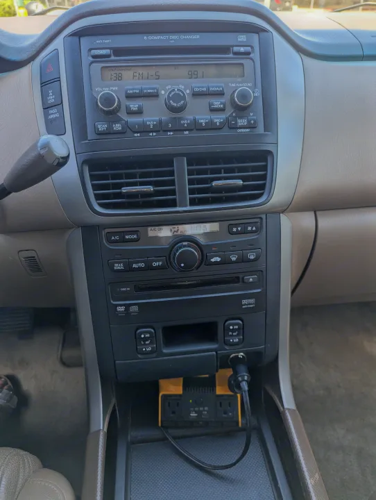 Inside an RV rental: car dashboard showing radio, climate controls, and a power inverter with USB and AC outlets for travel.. Honda Pilot 2007