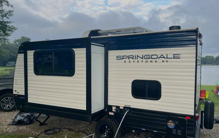 This Springdale Keystone RV rental, equipped with solar panels, is set up by a serene lake, ready for a camping getaway.. Keystone RV Springdale Mini 2025