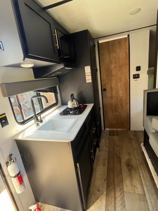 Experience an RV rental: a modern, compact kitchen with black cabinets, white counters, and wood-look flooring.. Keystone RV Springdale 2022
