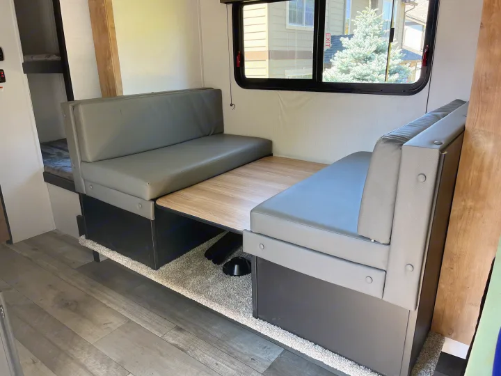 Inside an RV rental: a grey dinette with a wood table, window to outside, and a bunk bed area on the left.. Keystone RV Springdale 2022