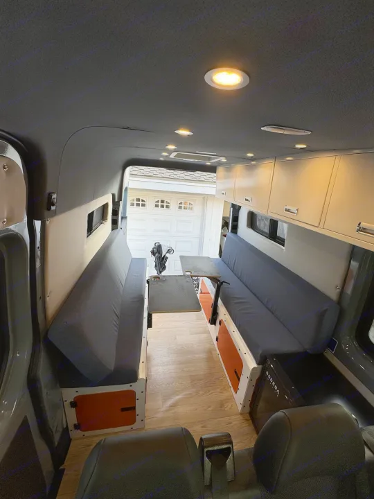 Inside a custom rv rental van conversion: comfortable living area with opposing cushioned benches, adjustable table, and overhead storage.. Mercedes Sprinter 2021