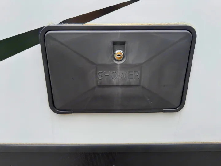 Exterior shower access panel on an RV rental. Dark grey cover with key lock & 'SHOWER' text, essential for outdoor cleaning.. Crossroads RV Volante 2021