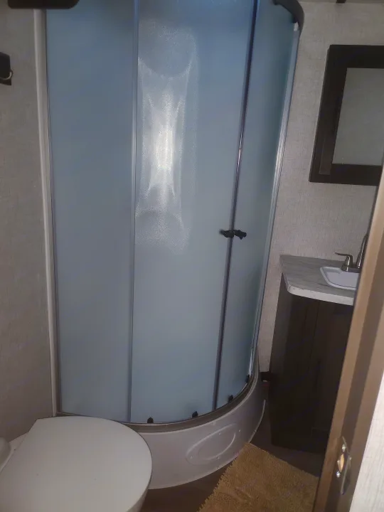 Compact RV rental bathroom featuring a curved frosted glass shower, toilet, and sink vanity.. Crossroads RV Cruiser Aire 2021