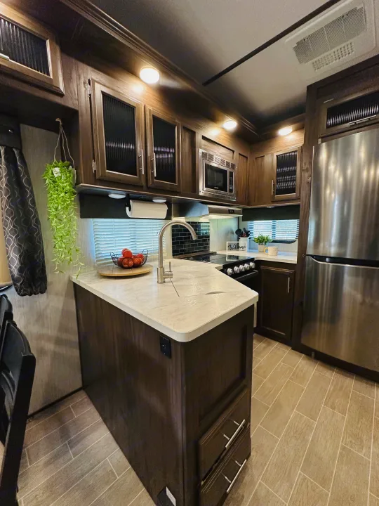Modern RV rental kitchen with dark wood cabinets, stainless steel appliances, a central island, and a clean aesthetic.. Forest River Cherokee Arctic Wolf 2019