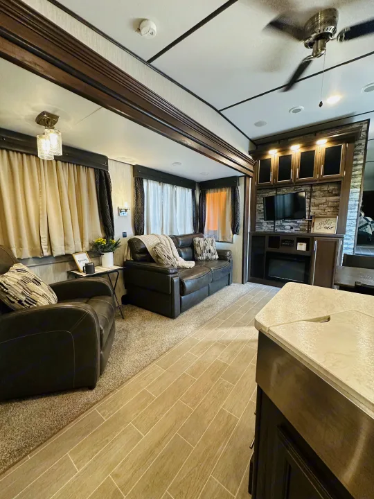 Modern RV rental interior: living room with sofa, armchair, TV, and kitchen counter visible. Features cozy decor.. Forest River Cherokee Arctic Wolf 2019