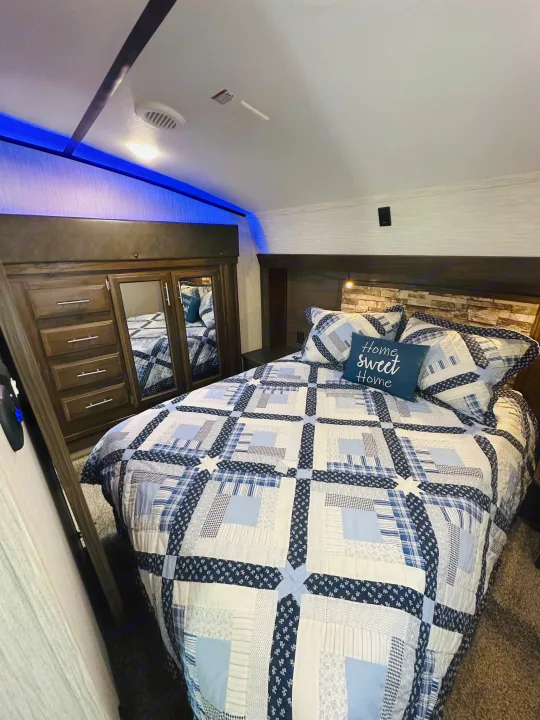 Comfortable RV rental bedroom with blue quilt, wooden storage, and ambient lighting, creating a cozy home-like interior.. Forest River Cherokee Arctic Wolf 2019