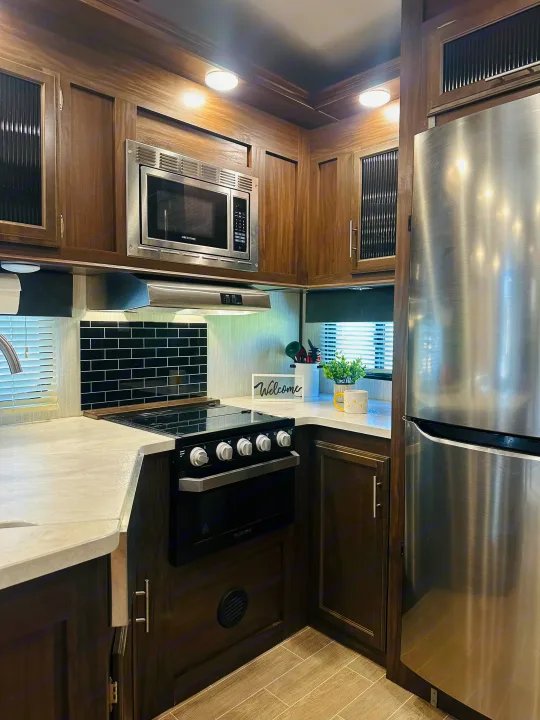 Well-appointed RV rental kitchen with stainless steel fridge, microwave, stove, dark cabinets & light counters.. Forest River Cherokee Arctic Wolf 2019