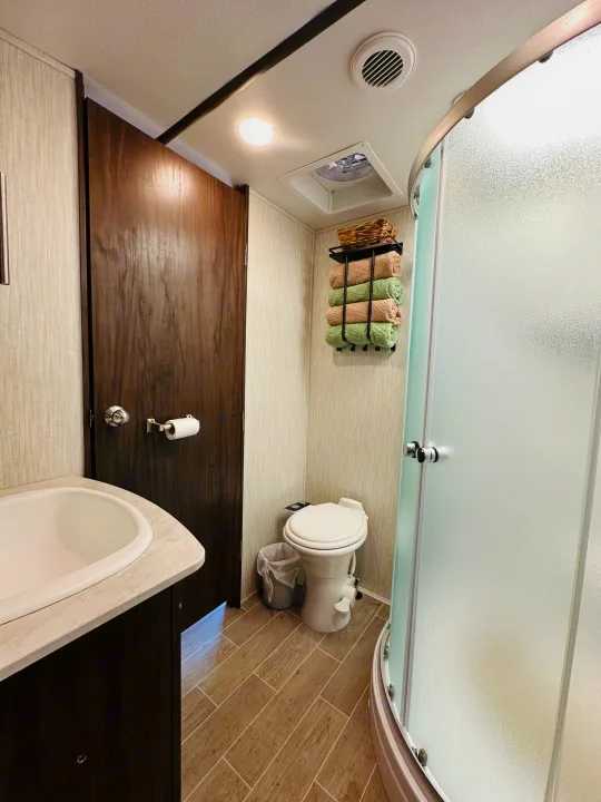 Clean RV rental bathroom with a compact sink, toilet, frosted shower, and towels on a wall rack.. Forest River Cherokee Arctic Wolf 2019