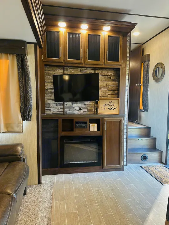 Spacious RV rental interior: entertainment center with TV, electric fireplace, "gather" sign, sofa, and inviting steps.. Forest River Cherokee Arctic Wolf 2019