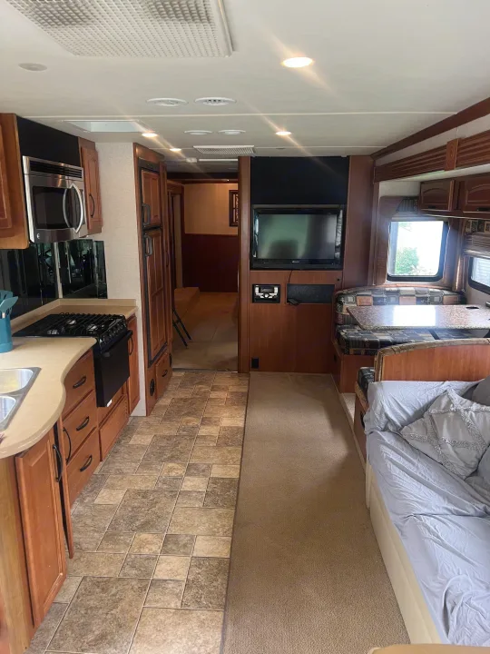 RV rental interior: well-equipped kitchen, cozy dining booth, and sleeping area. Features wood cabinets, appliances, tile, and carpet.. Fleetwood Fiesta LX 2010