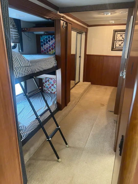RV rental: Bunk beds with ladder and striped bedding in a wood-paneled interior, leading to a mirrored closet and hallway.. Fleetwood Fiesta LX 2010