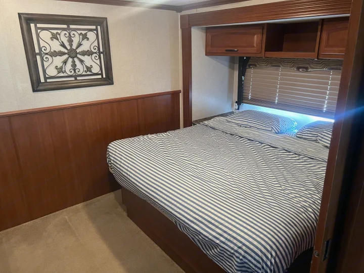 Comfortable RV rental bedroom with blue & white striped bed, wooden walls, and decorative metal art for a cozy travel stay.. Fleetwood Fiesta LX 2010