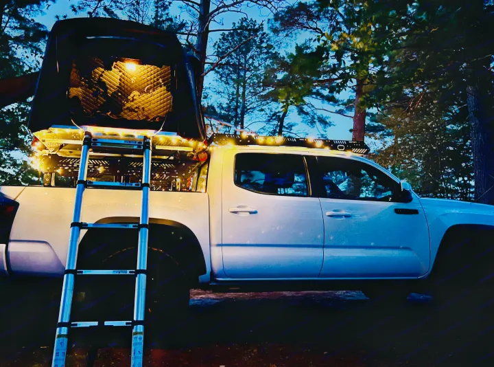 White pickup truck with illuminated rooftop tent, open, ladder extended. Great for overlanding or an RV rental adventure.. Toyota Tacoma TRD-Pro 2020