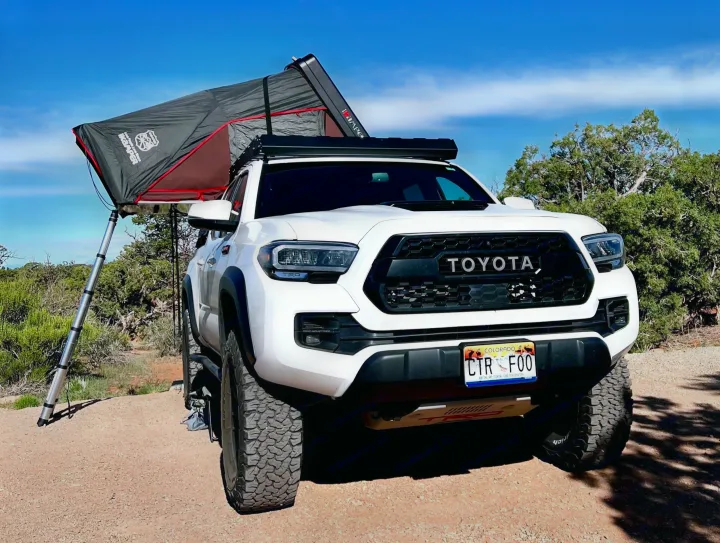 White Toyota Tacoma with rooftop tent deployed for overlanding, a rugged alternative to an RV rental for wilderness camping.. Toyota Tacoma TRD-Pro 2020