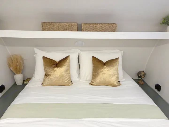Cozy RV rental bedroom featuring a comfy bed with white linens, gold pillows, a shelf with baskets, and decorative accents.. Heartland RVs Eddie Bauer Edition 17RB-C 2025