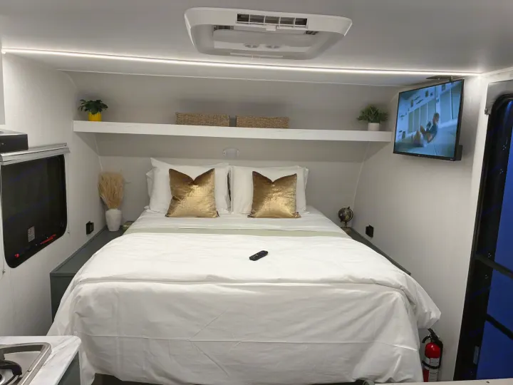 Cozy RV rental bedroom featuring a large bed, wall-mounted TV, AC unit, shelving, and essential safety features.. Heartland RVs Eddie Bauer Edition 17RB-C 2025