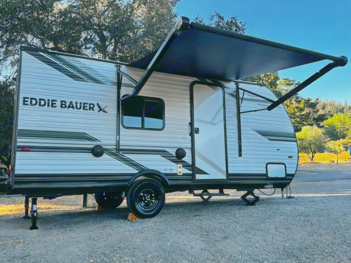 RV rental: An Eddie Bauer travel trailer is parked with its awning extended on a gravel site, amidst trees.. Heartland RVs Eddie Bauer Edition 17RB-C 2025