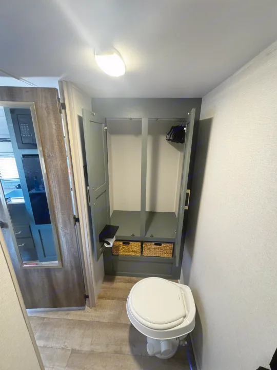 This RV rental interior shows a compact bathroom with a toilet, and an open wardrobe with shelving and baskets.. Heartland RVs Eddie Bauer Edition 17RB-C 2025
