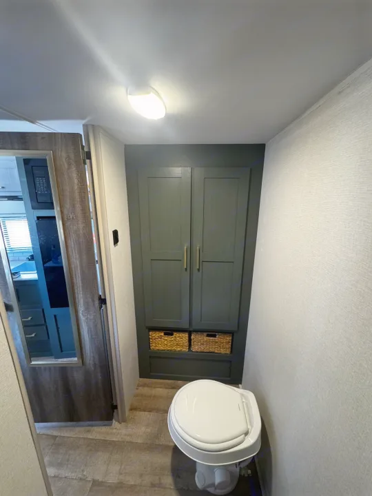 RV rental: A compact bathroom featuring a white toilet, dark green storage cabinet with baskets, and wood-look flooring.. Heartland RVs Eddie Bauer Edition 17RB-C 2025