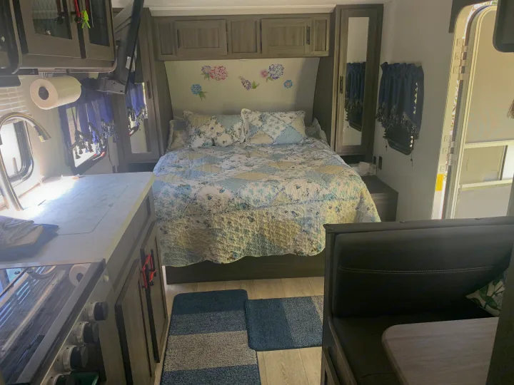 Cozy RV rental interior: kitchen with sink & stove, comfy bed with floral quilt, and dining area. Perfect for your next adventure!. Forest River Shasta 2021