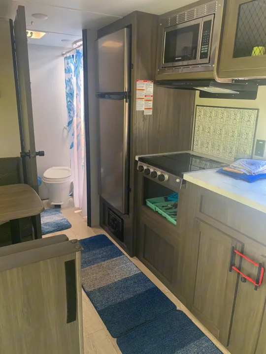 Inside this RV rental: compact kitchen with stove, microwave, fridge, and a small bathroom visible.. Forest River Shasta 2021