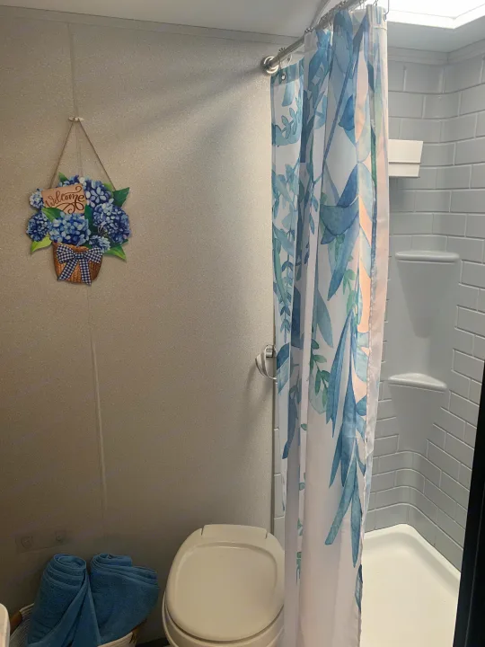 Cozy RV rental bathroom with a blue hydrangea welcome sign, shower, and toilet, offering comfort on the go.. Forest River Shasta 2021