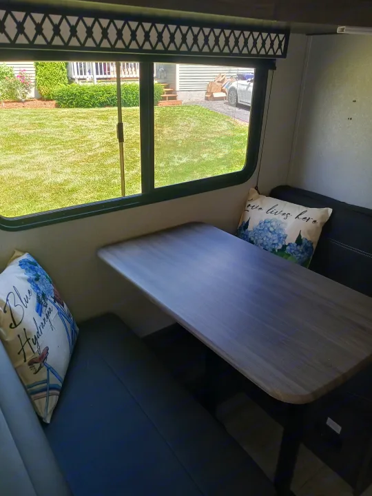 Enjoy the cozy dinette inside this rv rental, featuring comfy seating, decorative pillows, and a scenic outdoor view.. Forest River Shasta 2021