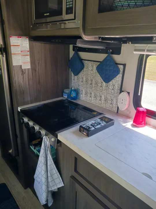 This RV rental kitchen features a stovetop, counter, Greystone microwave, backsplash, and kitchen essentials for your trip.. Forest River Shasta 2021
