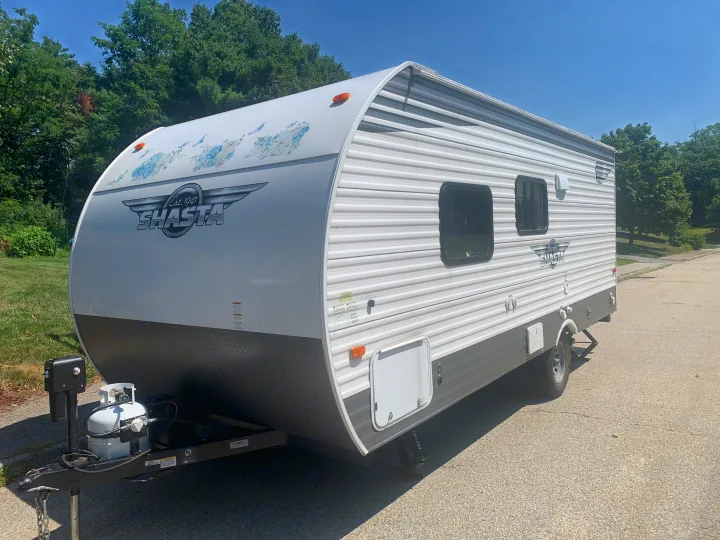 View of a white Shasta travel trailer, ideal for rv rental, showing its floral decals, windows, and front hitch setup.. Forest River Shasta 2021