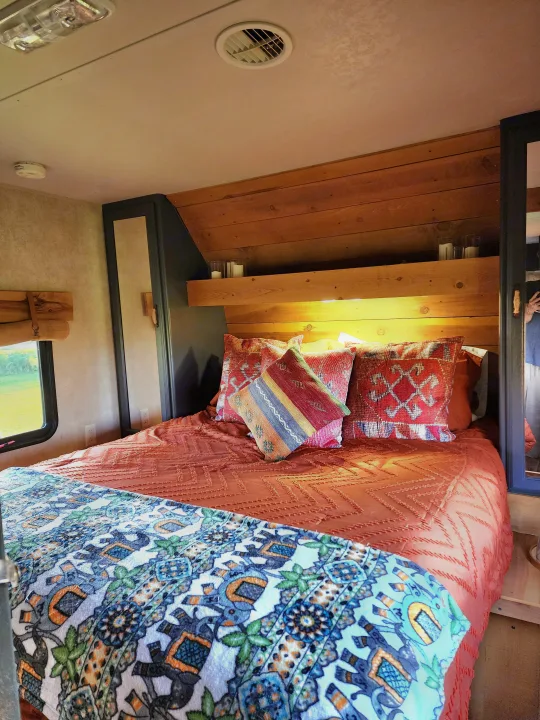Step into this cozy RV rental bedroom, boasting a wooden headboard, vibrant pillows, and patterned bedding.. Forest River Wildwood 2017